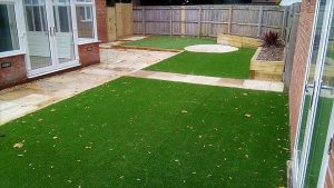 Large artificial grass area with stone path and patio area
